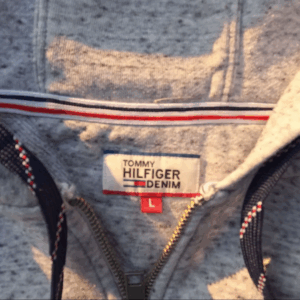 Close-up of a grey Tommy Hilfiger Denim zip-up hoodie showing the brand tag and signature neck tape, size large.